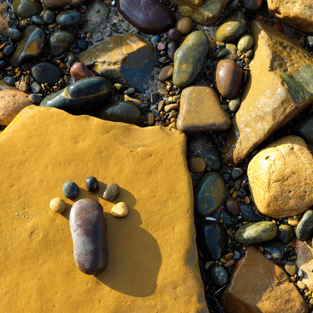 Lonely foot by pebble on rock background, amazing concept on stone surface with yellow color, art product at seasideの写真素材