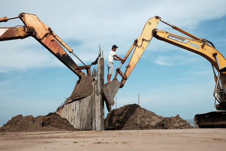 CA MAU, VIET NAM- JULY 16,2016: Vietnamese excavator driver control vehicle to build breakwater at beach to protect seaside from erosion at Camau, Vietnamのeditorial素材