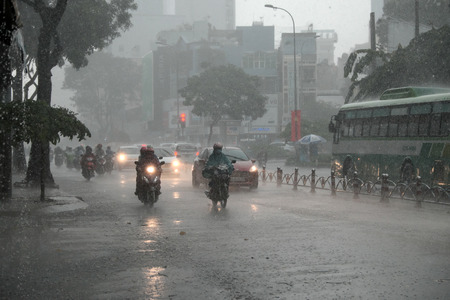 HO CHI MINH CITY, VIET NAM- AUG 28, 2016: Group of Vietnamese people wear helmet and raincoat ride motorbike in heavy rain, water on street, this time is rainy season at Saigon, Vietnamのeditorial素材