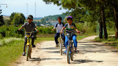 LAM DONG, VIET NAM-  DEC 28, 2016: Group of unidentified Vietnamese children ride bicycle on country road at noon, naughty boy run to tease his friend, Lamdong, Vietnamのeditorial素材