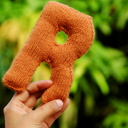 Woman hand pick knitted alphabet on green nature background, color handmade product knit from yarn with creative の写真素材