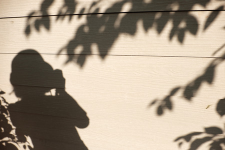 Sunny evening background, shadow of people and leaf on white wall of the house, silhouette woman take photo lonelyの写真素材