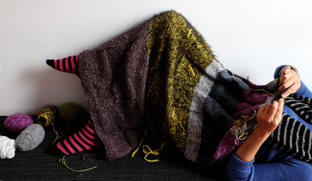 Asian woman lying on floor of home to knit woolen blanket for warm in wintertime, knitting is hobby...