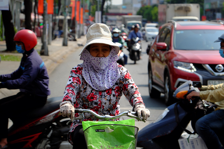 HO CHI MINH CITY, VIET NAM- APRIL 26: Vietnamese woman wear face mask to sun protection, ride bicycle under high temperature in hot day, tired face in extreme weather, Vietnamのeditorial素材