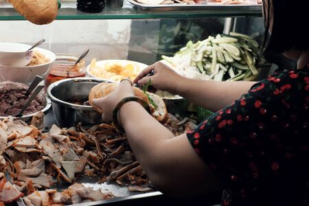 Vietnamese woman sell Vietnam bread on cart at night street food, stuffed food with meat, pork bologna, pickle, a famous and popular food that cheap, quick, Ho Chi Minh cityの写真素材