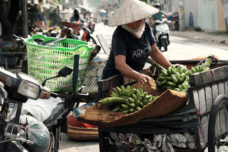 HO CHI MINH CITY, VIET NAM- JULY 06, 2019: Vietnamese woman transport many banana bunch by cart, female stand consider on bananas at roadside, close up scene with blurred background on dayのeditorial素材