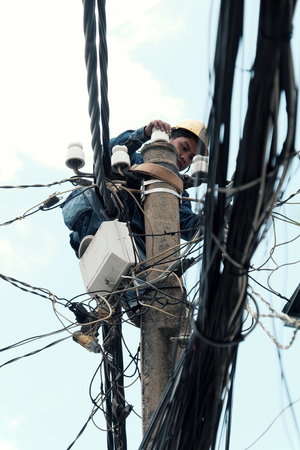 HO CHI MINH CITY, VIET NAM- JULY 12, 2019: Vietnamese electricity worker climb high on electric post to repair electricity network, man work in unsafe service at noon, Vietnamのeditorial素材