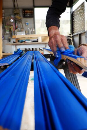 Vietnamese man working in workshop, male hands painting on wooden bar with blue paint coating,...
