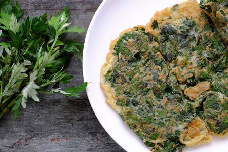 Healthy food from eggs with herbal, fried egg with mugwort leaves on white plate on wooden backgroundの写真素材