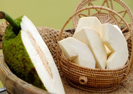 Close up breadfruit cut in half and slice in handmade basket on yellow background