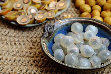 Top view Vietnamese tropical sweet, watery pulp fruit, close up Longan fruits flesh in translucent white on black plate with black seed, yellow peel, cut in half of dragon eye fruits backgroundの写真素材