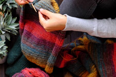 Top view woman feet with socks, sitting at home balcony, hand hold knitting needle to knit colorful wool scarf  for meaningful handmade winter gift when wintertime come.の写真素材