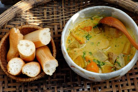 Delicious yellow vegan curry dish bowl with bread for breakfast from high view, vegetarian meal cook from taro, sweet potato, carrot, coconut milk and curry powder, homemade Vietnamese foodの写真素材