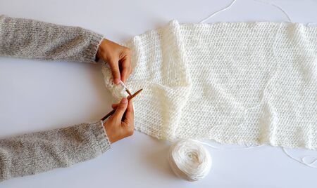 Top view simple concept for wintertime, woman hand with knitting needles to knit white scarf for handmade seasonal gift on white background, amazing gentles color の写真素材