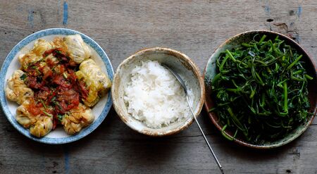 Simple Vietnamese vegan meal for lunch, boiled water spinach, stuffed cabbage with tomato sauce, bowl of rice on wooden background, healthy food that rich fiberの写真素材
