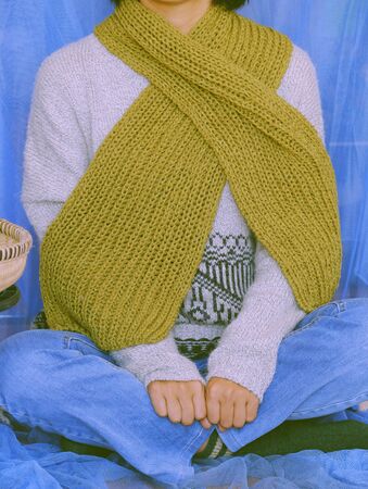 Woman wear blue jeans, white woolen sweater, sock and moss green wool scarf sit with blue background, knitted handmade product to make warm for winter as hobby in free timeの写真素材