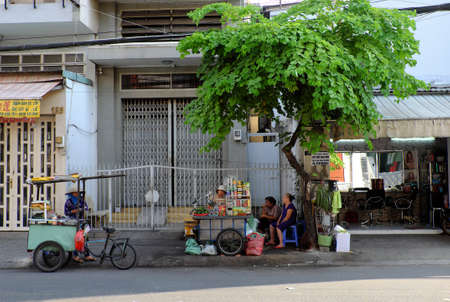 HO CHI MINH CITY, VIET NAM- JAN 5, 2020: Two peddle standing on sidewalk under branch of tree at noon, Vietnamese woman street vendor sell food and drink by handcart on urban roadのeditorial素材