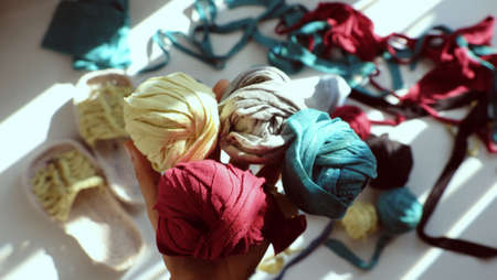 Close up from top view colorful scene in sunlight morning, woman hand hold group ball of yarn from recycle old t shirt on white background, fun leisure with homemade reuse by cut clothes in yarnsの写真素材