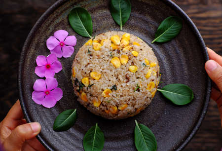 Top view plate of Vietnamese vegan fried rice with yellow corn on dark background, woman hand hold...