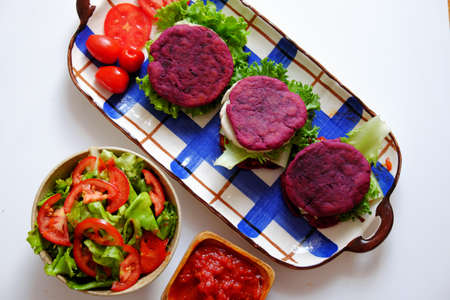 Amazing colorful raw material food for vegan hamburger from violet sweet potato with tomato sauce, salad, cucumber, healthy food for breakfast that rich starch, fiberの写真素材