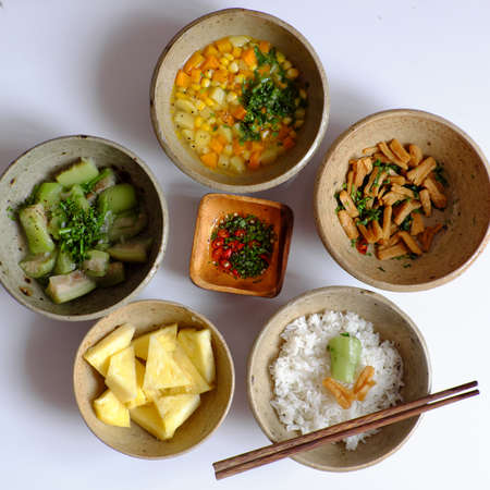 Top view Vietnamese daily meal for lunch time, tray of rice dish with melon, soup bowl from carrot, corn, potato, tofu skin fried, pineapple, sauce, vegan menu with non meat so good for healthの写真素材