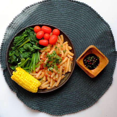 Top view simple vegan food for lunch, plate of pasta fried with leaf mustard and tomato sauce, yellow corn with soy sauce, quick vegetarian Vietnamese meal on white backgroundの写真素材