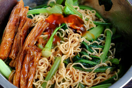 Quick and cheap vegan food for breakfast from instant noodles, fried with kale and tomato sauceの写真素材