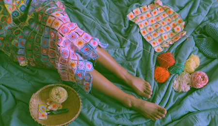 Top view woman legs with handmade product for warm in wintertime, crocheted colorful blanket by link many pieces artwork to make nice graphic shapes from yarn.の写真素材