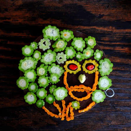 Top view colorful bitter melon sliced, green and ripe fruit cut in slice ready to cook on cutting board on dark wooden backgroundの写真素材