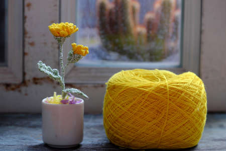 Beautiful artwork for home decor, crochet product to make yellow dandelion and green leaf with ball of yarn on wooden backgroundの写真素材
