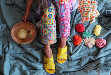 Top view woman legs with handmade product for warm in wintertime, crocheted colorful blanket by link many pieces artwork to make nice graphic shapes from yarn.の写真素材