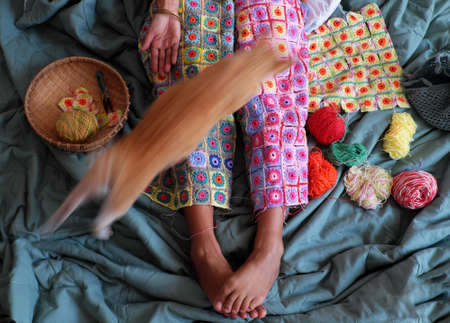 Top view woman legs with handmade product for warm in wintertime, crocheted colorful blanket by link many pieces artwork to make nice graphic shapes from yarn.の写真素材
