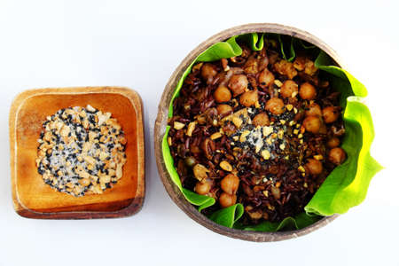 Vietnamese cuisine from red rice, delicious and nutrition rice dish for lunch, homemade food rich nutritious in coconut shell bowl with sesame salt on green leaf backgroundの写真素材