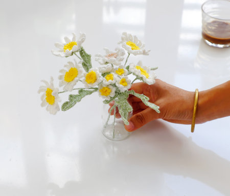 Woman hand hold handmade flower pot for home decor, white petal daisy and yellow pistil crochet from yarn at leisure activities on white backgroundの写真素材