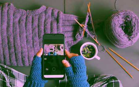 Top view woman hand wear blue mitten crochet, knit violet sweater for gift in wintertime, close hand press smartphone to take photo on dark toneの写真素材