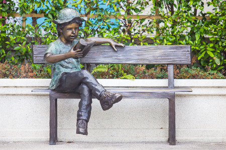 Boy statue is reading a book on the chair.の写真素材
