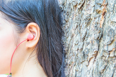 Pretty women or girl using ear headphone to listen song in public park.