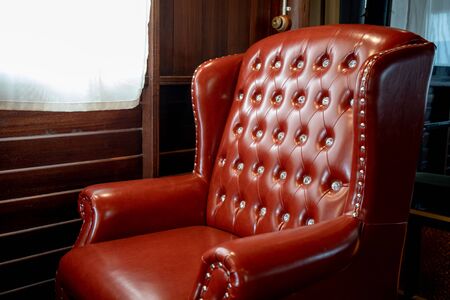 Closeup of vintage leather red chair in room near window.