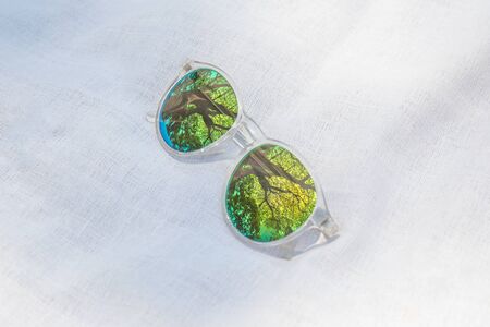 White plastic fashion glass on white fabric in the public park with reflection with green tree in forest.の写真素材