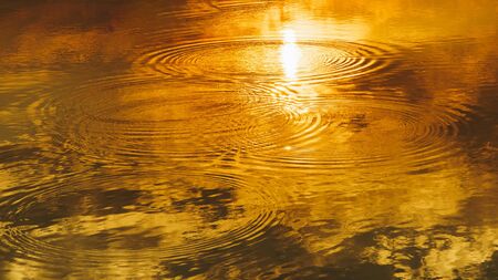 Water ripple circle on the surface of lake water with reflection of sky clouds at sunset or evenig time.の写真素材