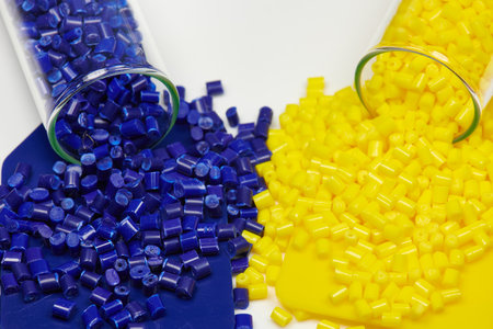 Blue and yellow plastic beads in a test tube on white background. Colored plastic resins in test tubes in laboratory with color samples and patternの写真素材