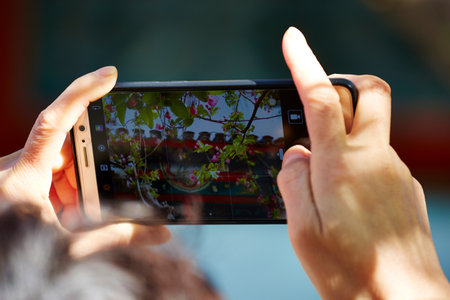 Two hands holding a smartphone to photograph flowers, capturing the essence of spring.