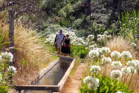FUNCHAL, PORTUGAL - JULY 15, 2017: Hiking group at sunny day along a path of flowers and the levada