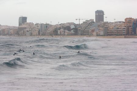 Local kids on surf boards waiting for the perfect wave to surf in the middle of the city of Las Palmas de Gran Canariaの写真素材