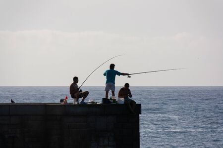 Maspalomas, Spain - Sep 17, 2010: At the end of the pier of Maspalomas lighthouse are tree fisherman busy early in the morning to catch fish.のeditorial素材