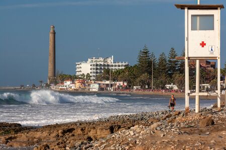 Maspalomas, Spain - Jan 2, 2011: Maspalomas lighthouse and beach. In the sea high waves. A woman is walking and the is a red cross buildingのeditorial素材