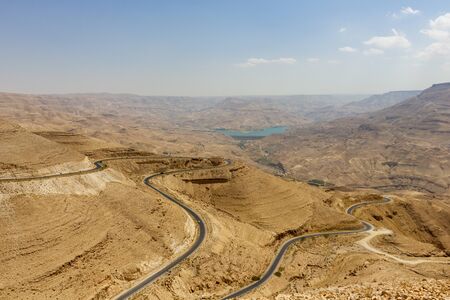 View of the Wadi Mujib where a long and winding road leads to the dam where a large lake is formed behind. The Wadi Mujib is aka the biblical Arnon Stream and is a river canyon that enters the Dead Seaの写真素材