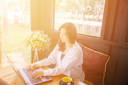 An Asian girl is typing and looking to the notebook keyboard on the wooden table.の写真素材