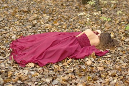 a girl in a red dress lying on the fallen leavesの写真素材