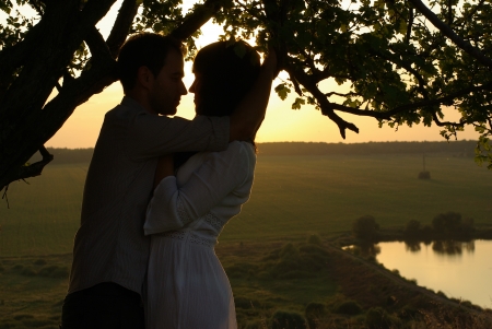 Couple kissing under tree at summer eveningの写真素材